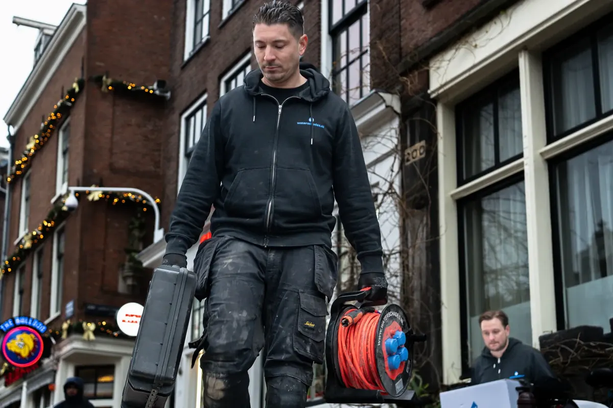 Specialist van Waterschades.nl loopt met apparatuur naar een pand in Amsterdam